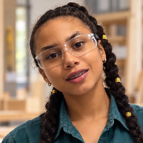 Carpentry student in safety glasses holding blueprints in a woodshop