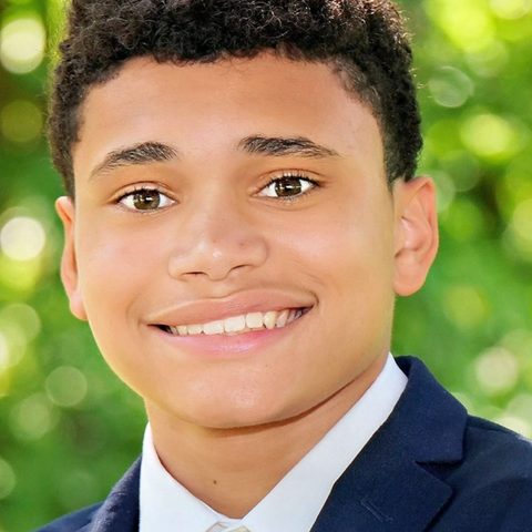 Student in a navy blazer and striped tie smiling outdoors